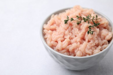 Photo of Fresh raw minced meat and thyme in bowl on light grey table, closeup. Space for text