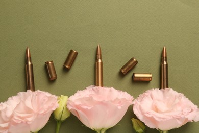 Bullets, cartridge cases and beautiful eustoma flowers on green background, flat lay. Space for text