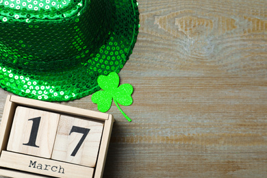 Green leprechaun hat, clover leaf and wooden block calendar on table, flat lay with space for text. St. Patrick's Day celebration