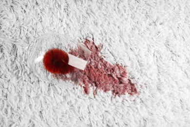 Photo of Overturned glass and spilled exquisite red wine on soft carpet, top view