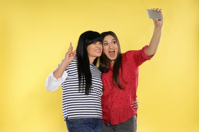 Young woman and her mother taking selfie on color background