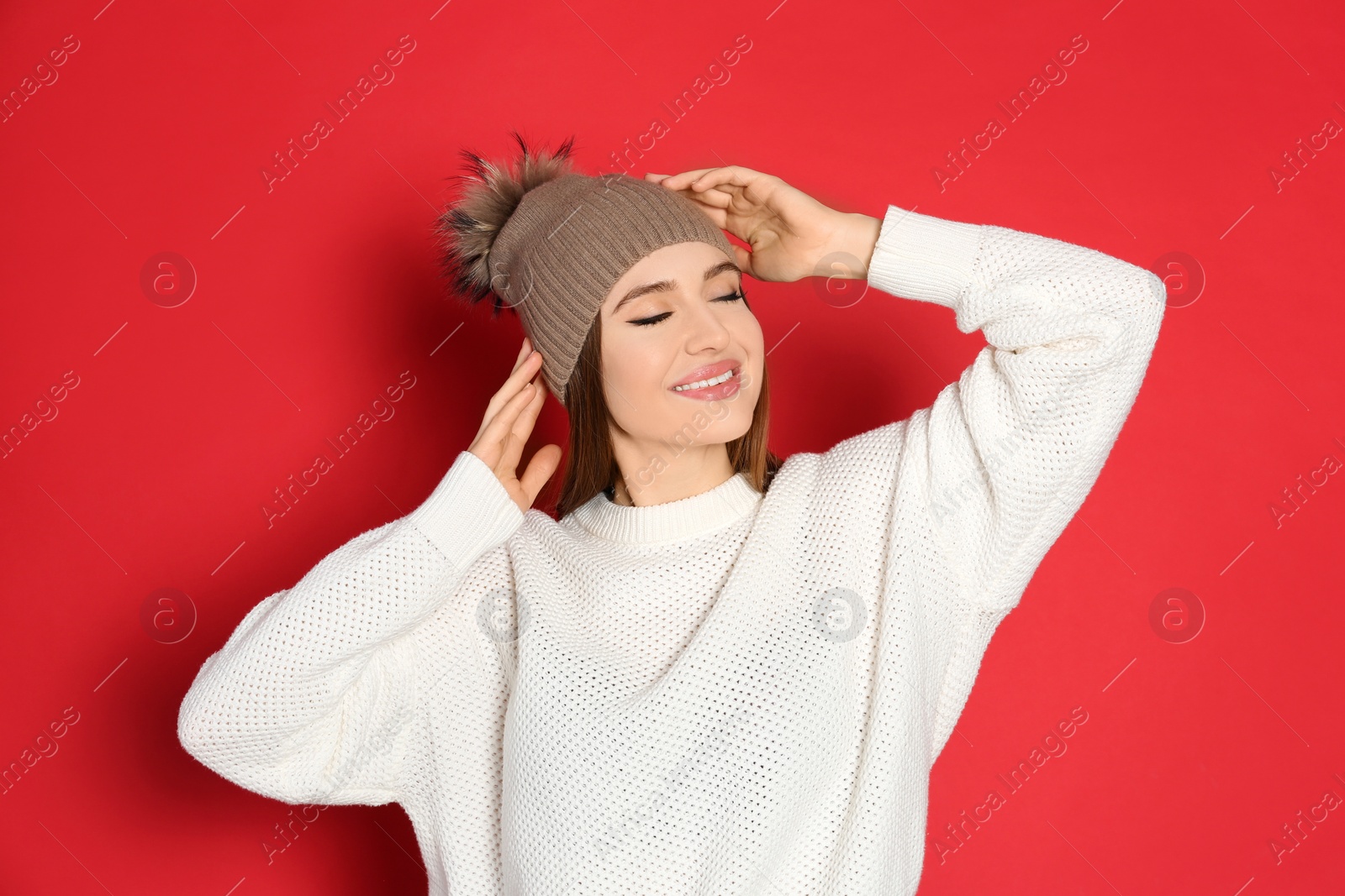 Photo of Young woman wearing warm sweater and hat on red background. Winter season