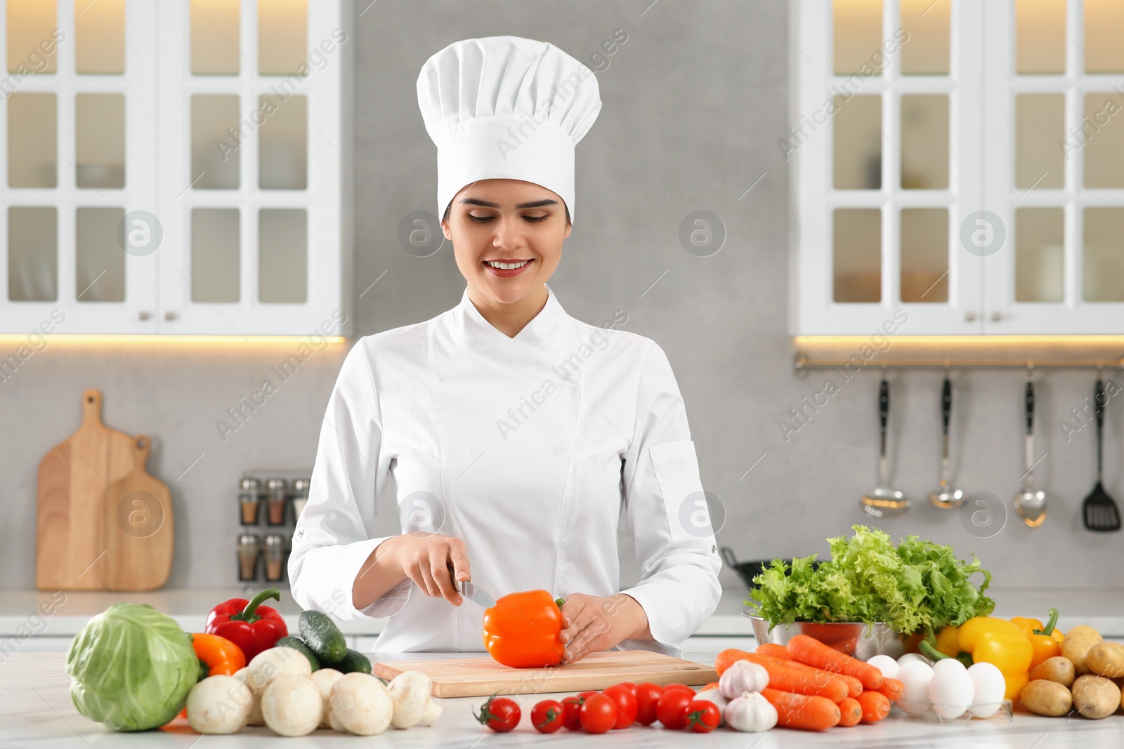 Photo of Professional chef cutting cut bell pepper at white marble table in kitchen