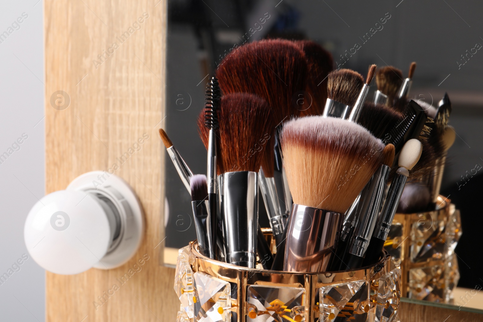 Photo of Set of professional makeup brushes near mirror on wooden table, closeup