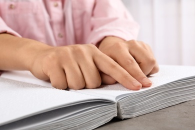 Photo of Blind person reading book written in Braille at table, closeup