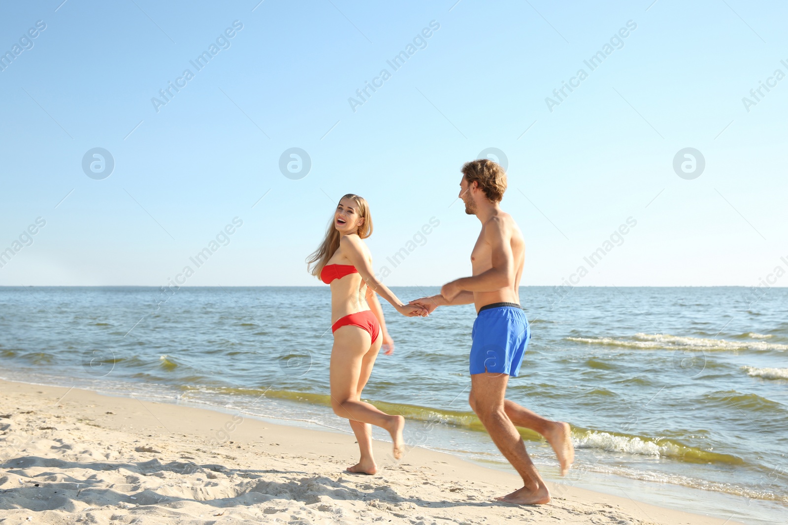 Photo of Happy young couple in beachwear running together on seashore