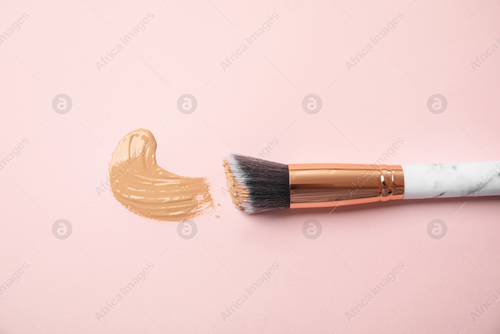 Photo of Sample of liquid foundation and makeup brush on pink background