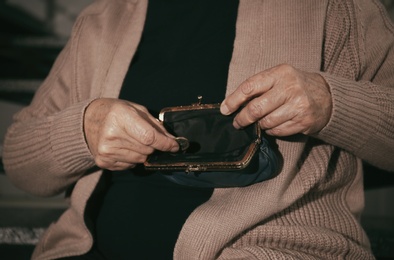 Poor senior woman with empty wallet and coin indoors, closeup