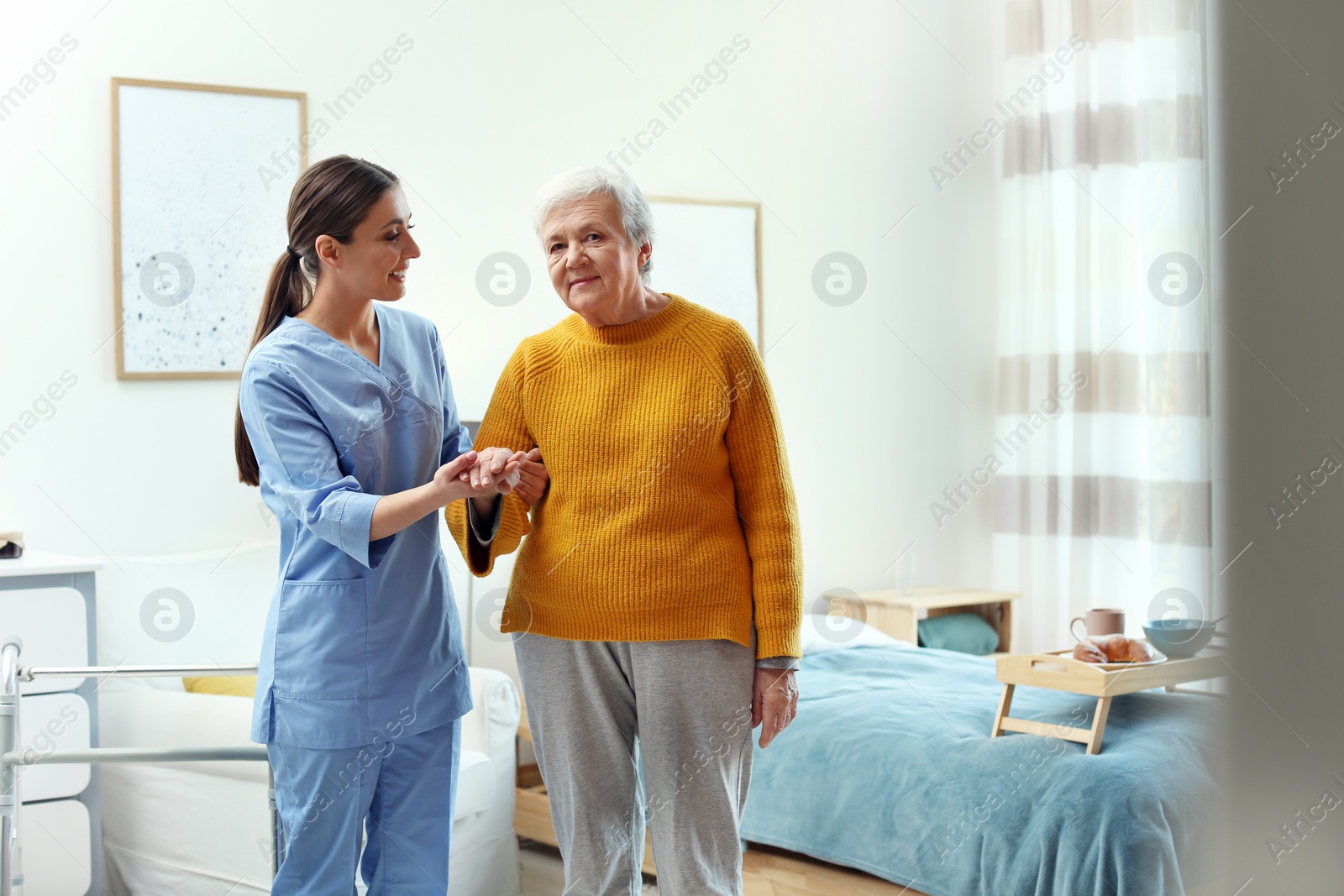 Photo of Care worker helping elderly woman to walk in geriatric hospice