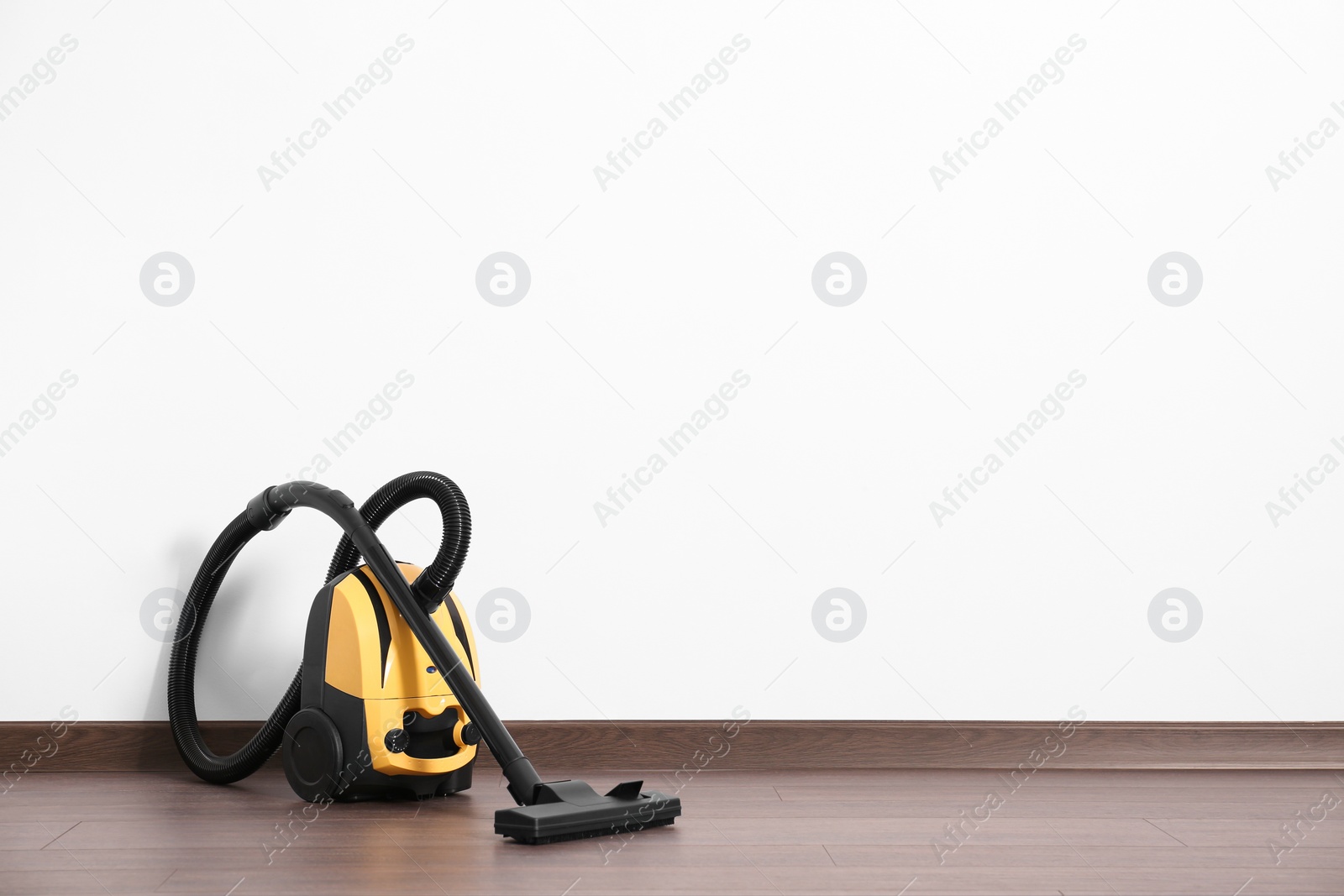 Photo of Modern yellow vacuum cleaner on wooden floor near white wall, space for text