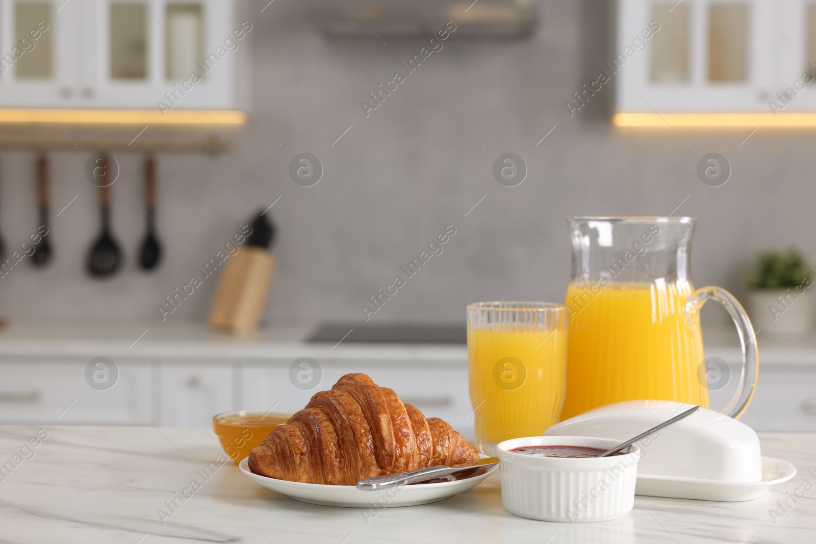 Photo of Breakfast served in kitchen. Fresh croissant, jam, honey and orange juice on white table. Space for text