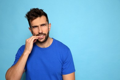 Man biting his nails on light blue background. Space for text