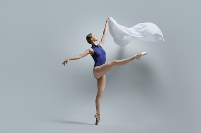 Graceful young ballerina practicing dance moves with veil on grey background