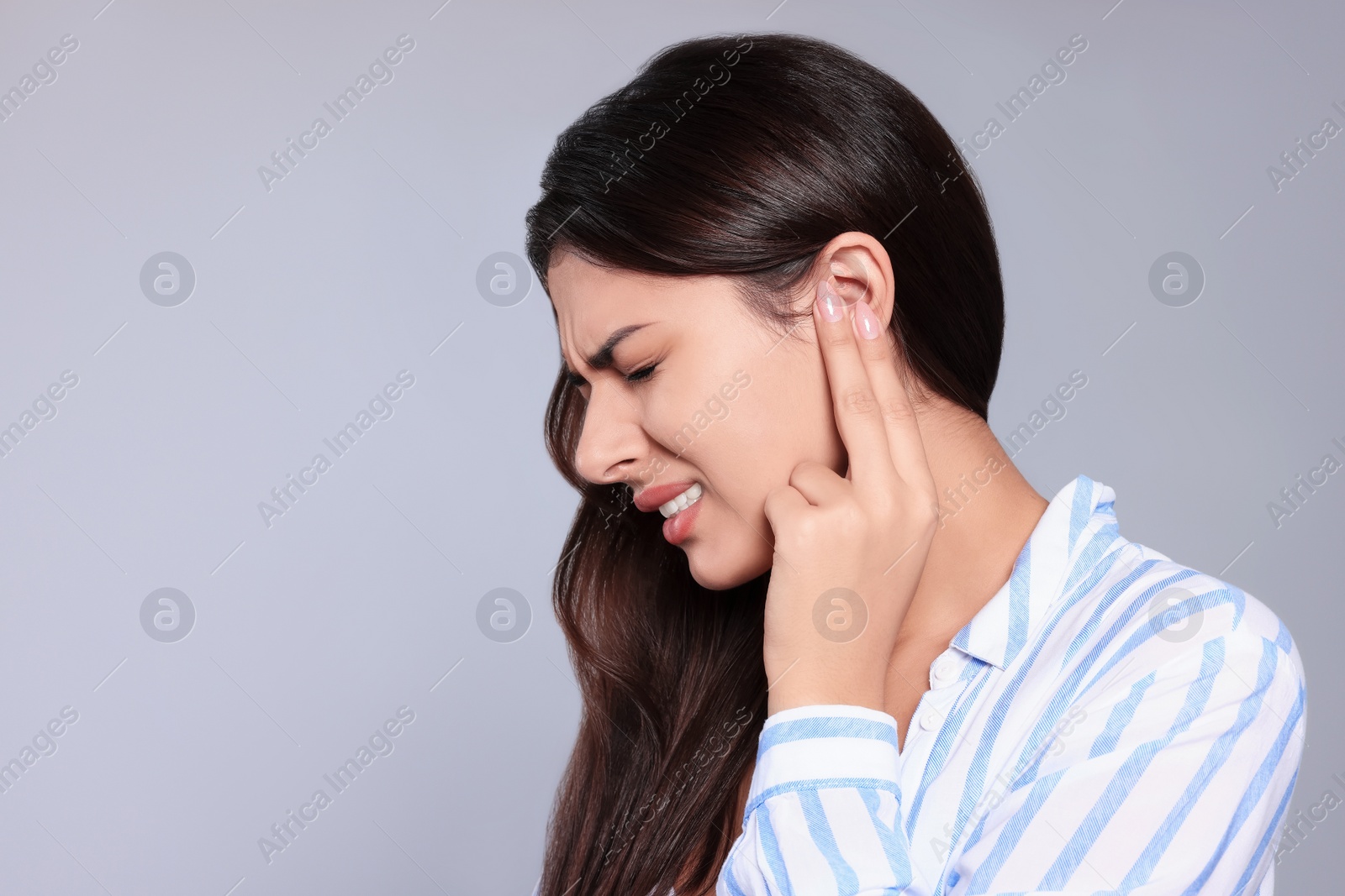 Photo of Young woman suffering from ear pain on light grey background, space for text