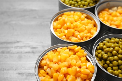 Photo of Open tin cans of conserved vegetables on grey background, closeup. Space for text