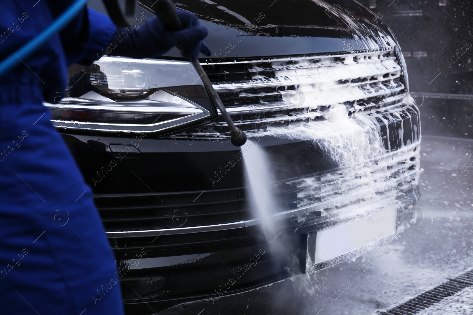 Photo of Worker cleaning automobile with high pressure water jet at car wash, closeup