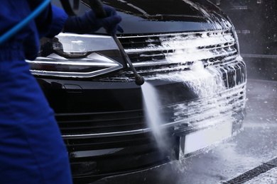 Photo of Worker cleaning automobile with high pressure water jet at car wash, closeup