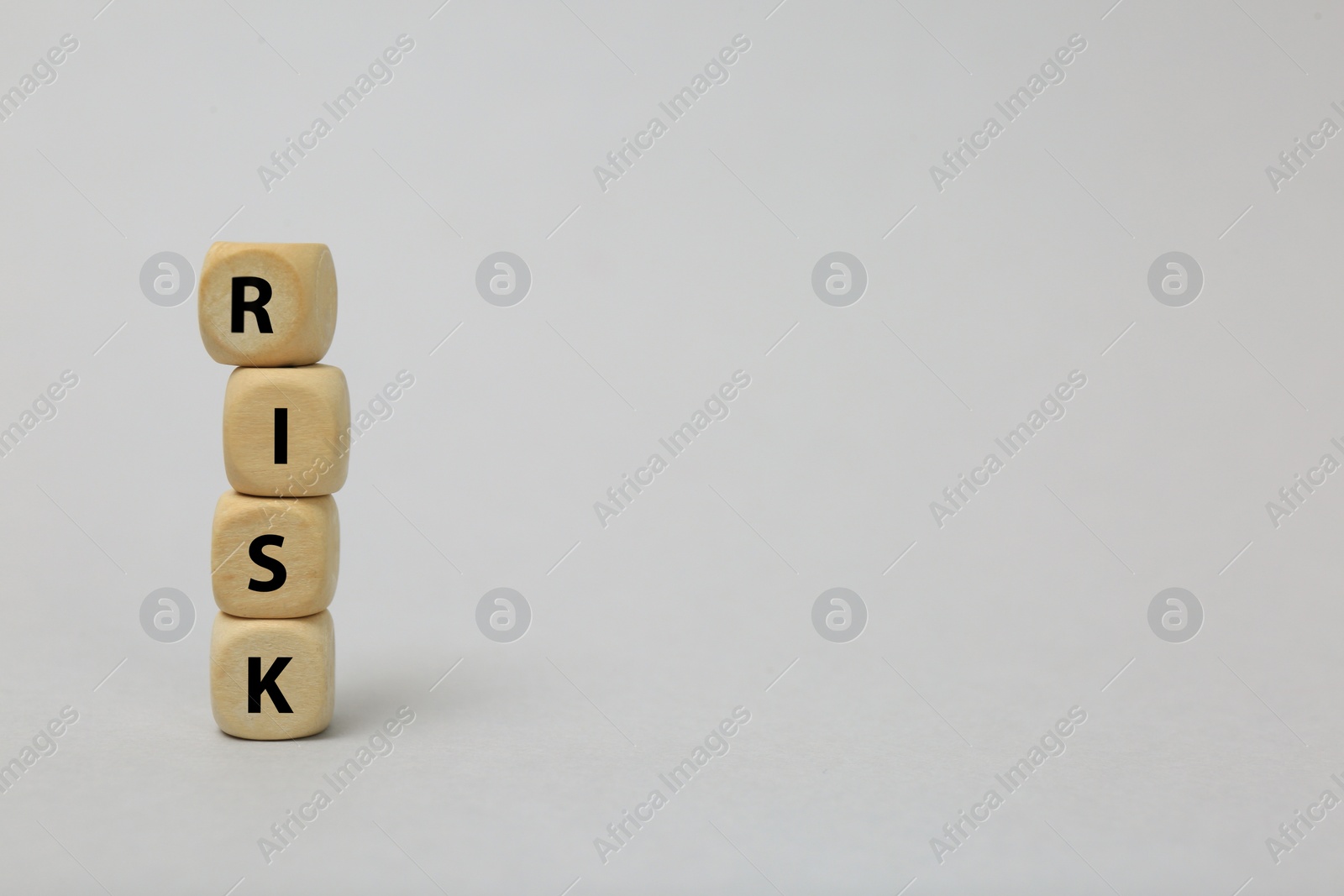 Photo of Stack of wooden cubes with word Risk on light grey background. Space for text