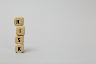 Photo of Stack of wooden cubes with word Risk on light grey background. Space for text