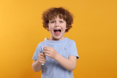 Photo of Cute little boy holding electric toothbrush on yellow background