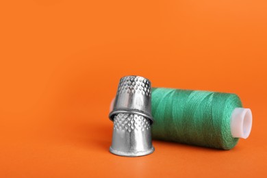 Thimbles and spool of green sewing thread on orange background, closeup. Space for text