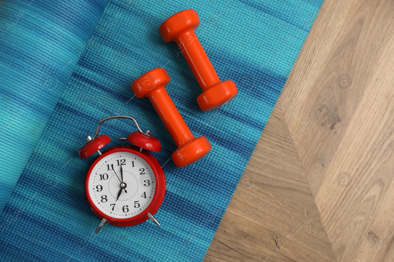 Photo of Alarm clock, yoga mat and dumbbells on wooden background, flat lay. Morning exercise