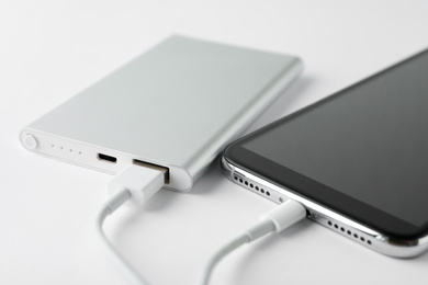 Smartphone charging with power bank on white background, closeup