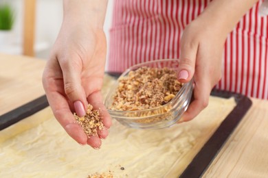 Photo of Making delicious baklava. Woman adding chopped nuts to dough at wooden table, closeup