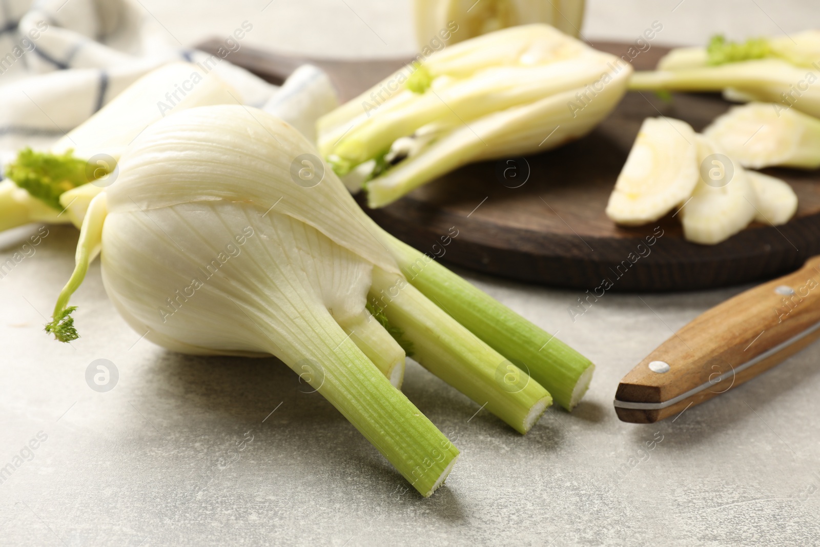 Photo of Whole and cut fennel bulb on light gray table, closeup