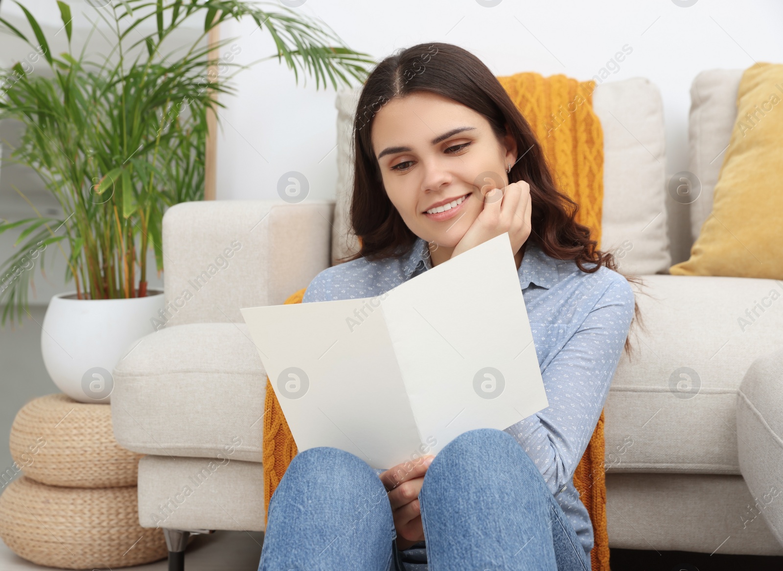 Photo of Young woman with greeting card on floor in living room