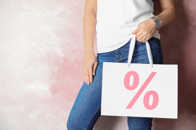 Image of Woman holding paper shopping bag with percent sign near pink wall, closeup. Discount concept