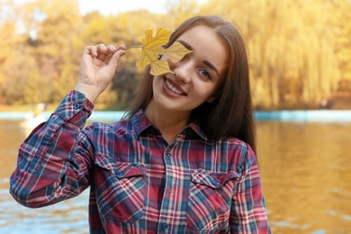 Young beautiful woman with leaf near pond in park. Autumn walk