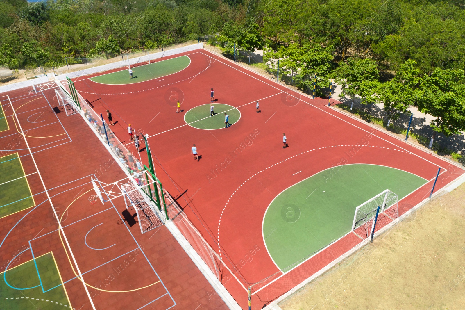 Image of Children playing soccer at outdoor sports complex on sunny day, aerial view