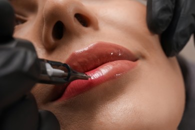 Young woman undergoing procedure of permanent lip makeup in tattoo salon, closeup