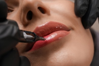 Photo of Young woman undergoing procedure of permanent lip makeup in tattoo salon, closeup