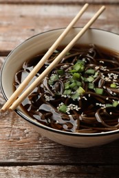 Photo of Tasty soup with buckwheat noodles (soba), onion in bowl and chopsticks on wooden table, closeup