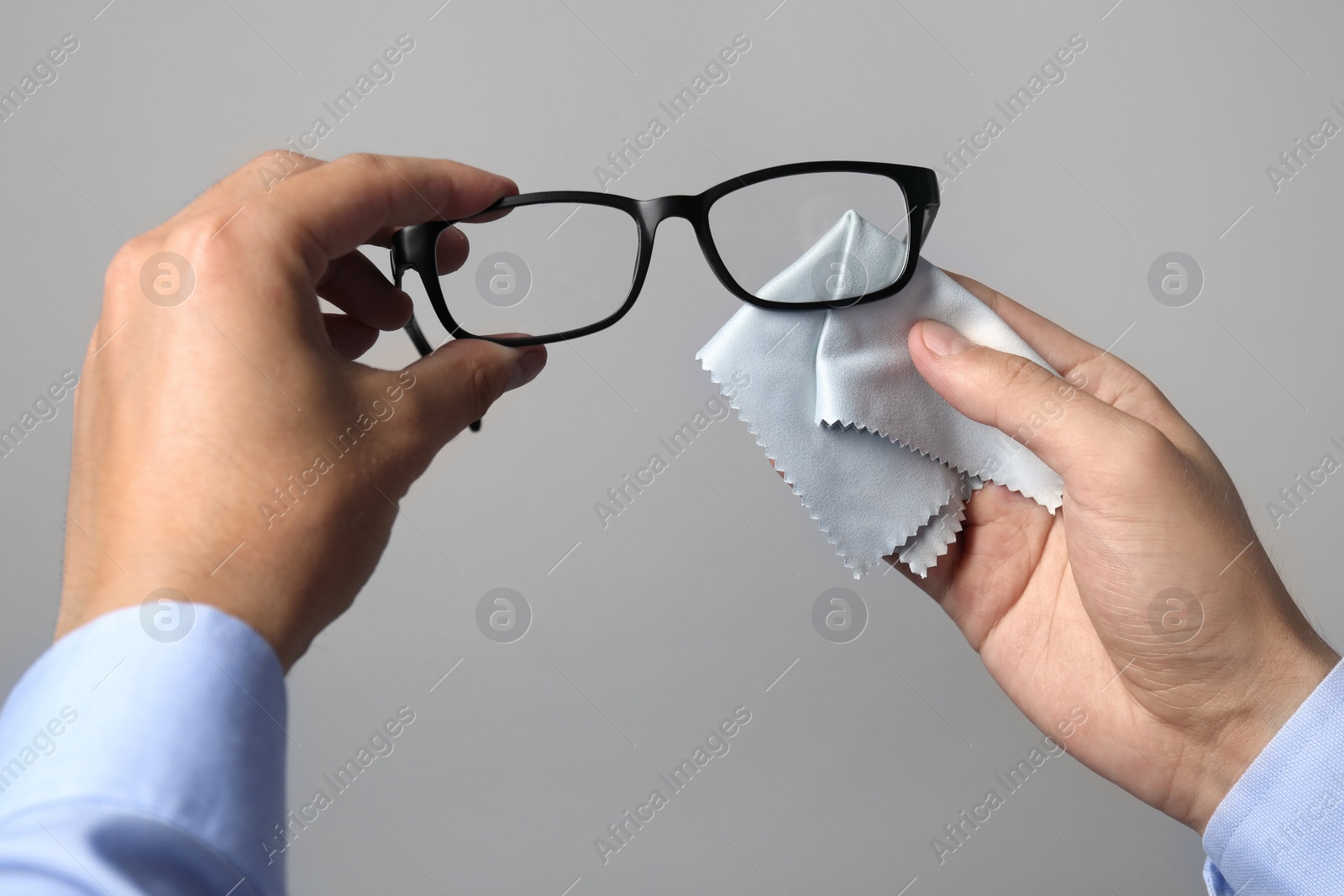 Photo of Man wiping glasses with microfiber cloth on light grey background, closeup