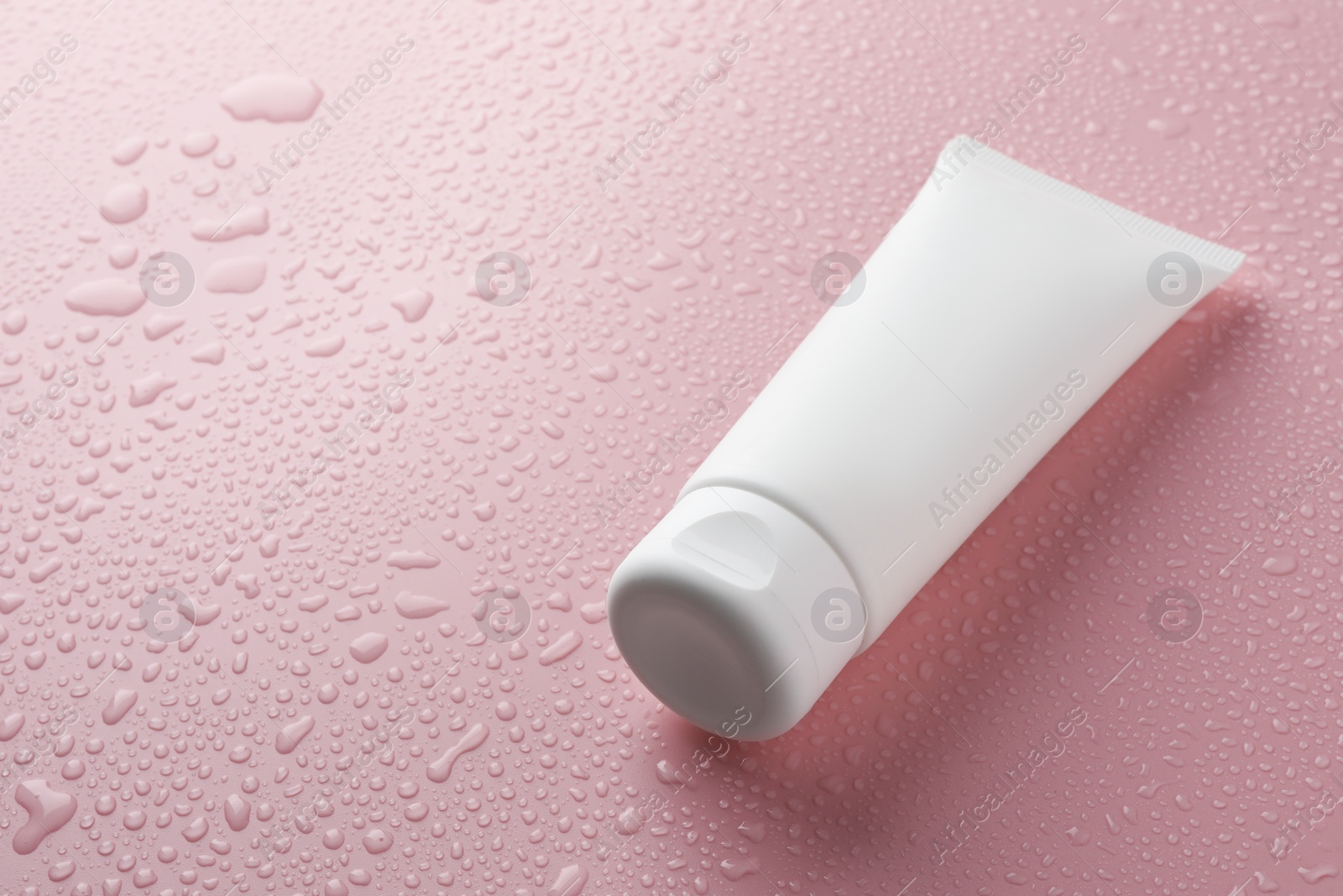 Photo of Moisturizing cream in tube on pink background with water drops, closeup. Space for text