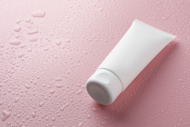 Moisturizing cream in tube on pink background with water drops, closeup. Space for text