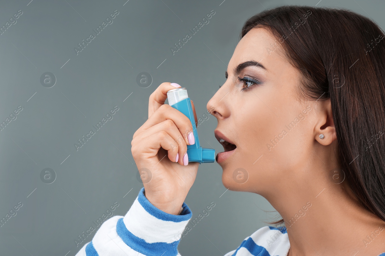 Photo of Young woman using asthma inhaler on color background