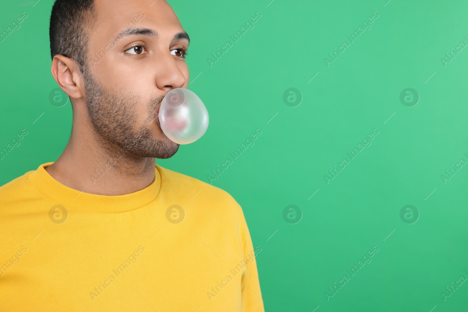 Photo of Young man blowing bubble gum on green background. Space for text