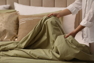 Photo of Woman making bed with olive green linens, closeup