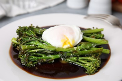 Tasty cooked broccolini with poached egg and sauce on plate, closeup