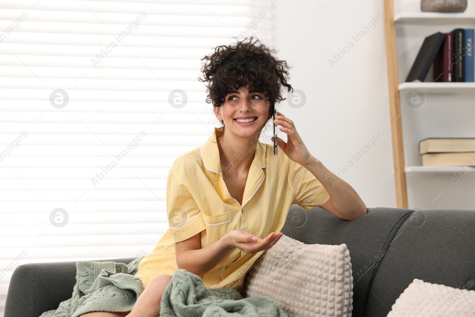 Photo of Beautiful young woman in stylish pyjama talking on smartphone on sofa at home