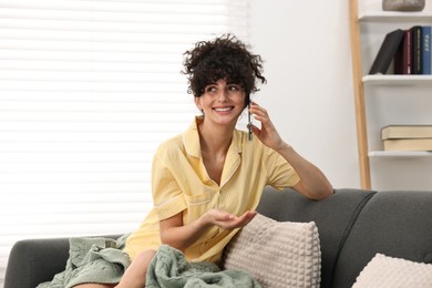 Photo of Beautiful young woman in stylish pyjama talking on smartphone on sofa at home