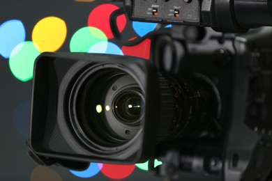 Photo of Modern video camera against blurred colorful lights, closeup