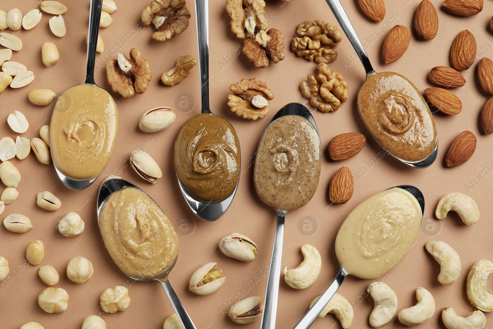 Photo of Tasty nut butters in spoons and raw nuts on light brown table, flat lay