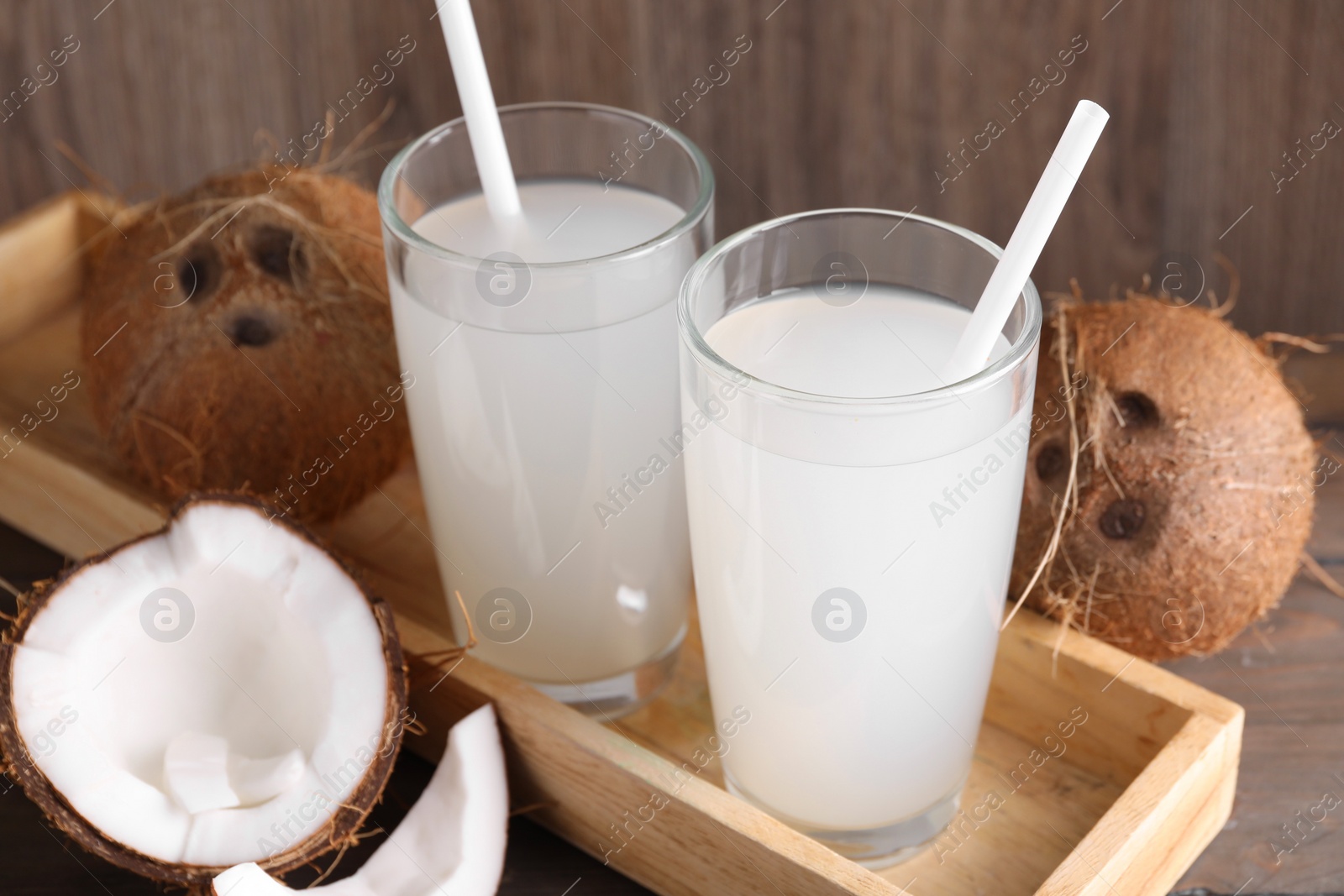 Photo of Glasses of coconut water with straws and nuts on wooden table