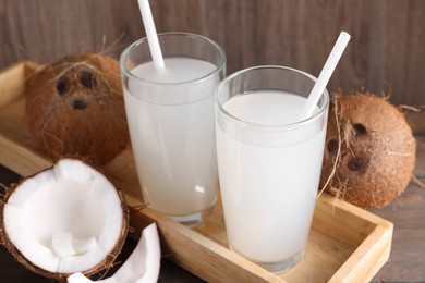 Glasses of coconut water with straws and nuts on wooden table