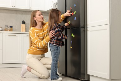 Photo of Mom and daughter putting magnetic letters on fridge at home. Learning alphabet